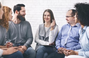 Smiling Psychologist Talking To Group Members At Therapy Session In Rehab